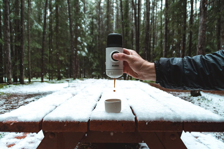 Ein Getränk aus einer Thermoskanne in eine Tasse auf einem schneebedeckten Picknicktisch im Wald gießen.