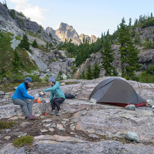 Zwei Camper bereiten neben ihrem MSR® Ultraleichtes FreeLite™ 1 „V2“ 1-Personen-Backpacking-Zelt in einer bergigen Landschaft eine Mahlzeit zu.