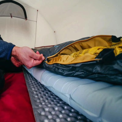 Eine Person öffnet eine Therm-a-Rest® NeoAir® XTherm™ NXT MAX Isomatte auf einer Isomatte mit ausgezeichnetem Wärme-Gewicht-Verhältnis innerhalb eines Zeltes.