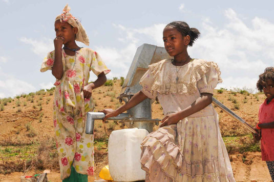 Kinder füllen Wasserkanister an einer Pumpe in ländlicher Umgebung.