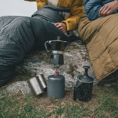 Zwei Camper sitzen mit einem Robens® Schlafsack Serac 600 -14°C Herd und brühen im Freien Kaffee.