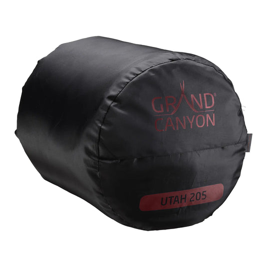 Schwarz-roter Grand Canyon® Utah 205 – Schlafsack zusammengerollt und in einem Kompressionssack mit „Grand Canyon“-Logo aufbewahrt.