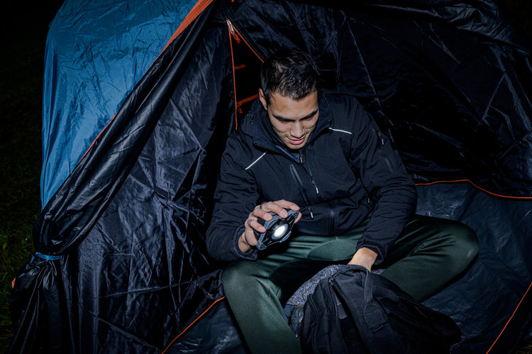 Eine Person untersucht einen Gegenstand mit einer Taschenlampe, während sie nachts in einem Zelt sitzt.