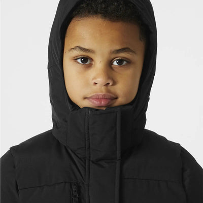 Kind trägt einen schwarzen Adore Puffy Parka von Helly Hansen® Juniors mit Reißverschlusskragen.