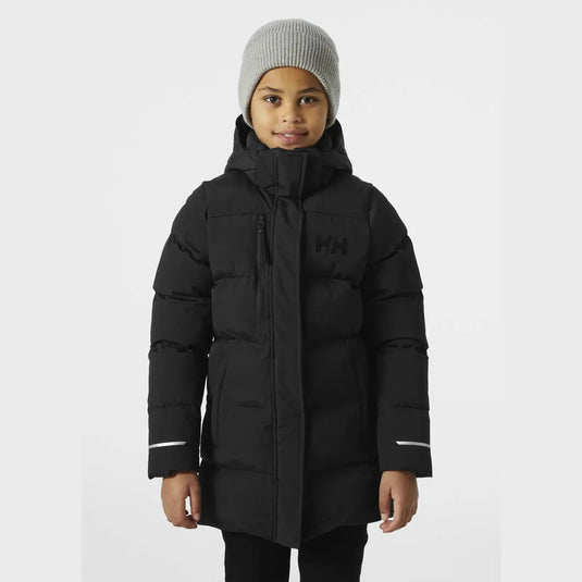 Kind trägt einen schwarzen wattierten Wintermantel „Adore Puffy Parka“ von Helly Hansen® Juniors und eine graue Mütze.