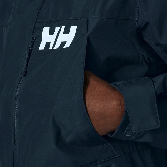 Nahaufnahme eines dunklen, isolierten Helly Hansen® Men’s Rigging Insulated Raincoat mit einem weißen Helly Hansen®-Logo und dem Ellbogen einer Person, der aus einer offenen Belüftungsöffnung herausragt.