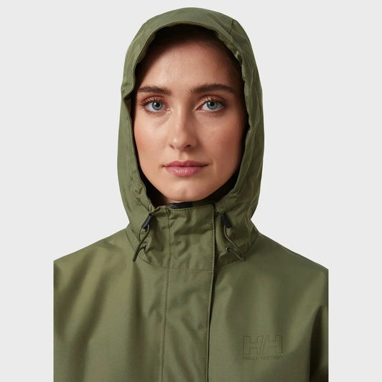 Frau trägt eine grüne wasserdichte Helly Hansen® Women's Seven J Regenjacke mit dem „Helly Hansen“-Logo.