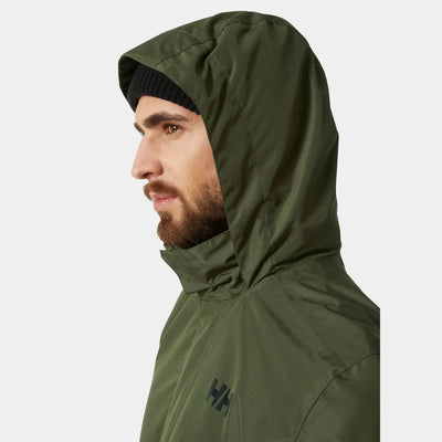 Ein Mann trägt eine grüne wasserdichte Herrenjacke „Dubliner“ von Helly Hansen® mit einem sichtbaren Logo auf der Vorderseite.