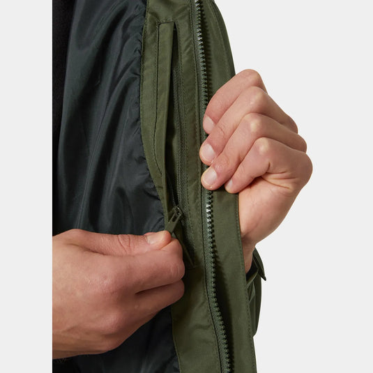 Eine Nahaufnahme der Hand einer Person, die den Reißverschluss einer grünen wasserdichten Dubliner-Herrenjacke von Helly Hansen® zuzieht.