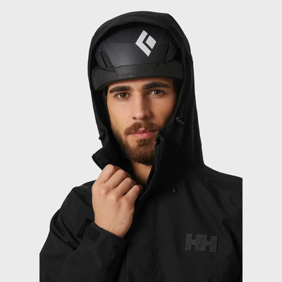 Mann trägt eine schwarze Banff-Shelljacke für Herren von Helly Hansen® und einen Skihelm.