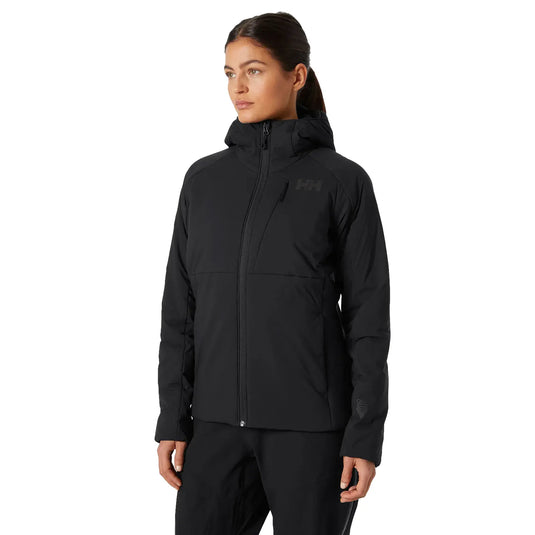 Eine Frau trägt eine schwarze Damenjacke „Odin Stretch Hood Insulator 2.0“ von Helly Hansen mit dem Odin Stretch Hood-Logo auf der Brust.