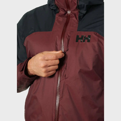 Nahaufnahme einer Person, die eine kastanienbraune und schwarze Helly Hansen® Men’s Verglas 2L Shell Jacket trägt, wobei der Reißverschluss teilweise geöffnet ist.