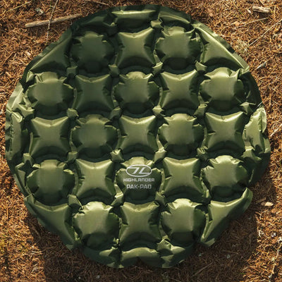 Aufblasbares HIGHLANDER® PAK-PAD aufblasbares Sitzkissen, Olive, Campingunterlage auf dem Boden platziert.