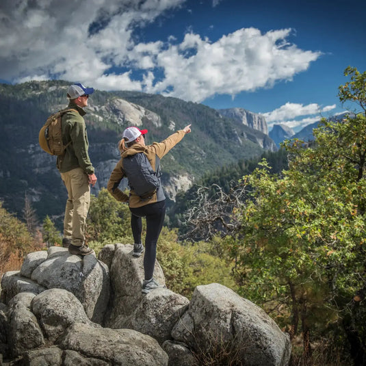 Zwei Wanderer, einer in einer Helikon-Tex® Womens Cumulus Jacke – Heavy Fleece, stehen auf felsigem Gelände, einer zeigt auf eine Berglandschaft unter bewölktem Himmel.