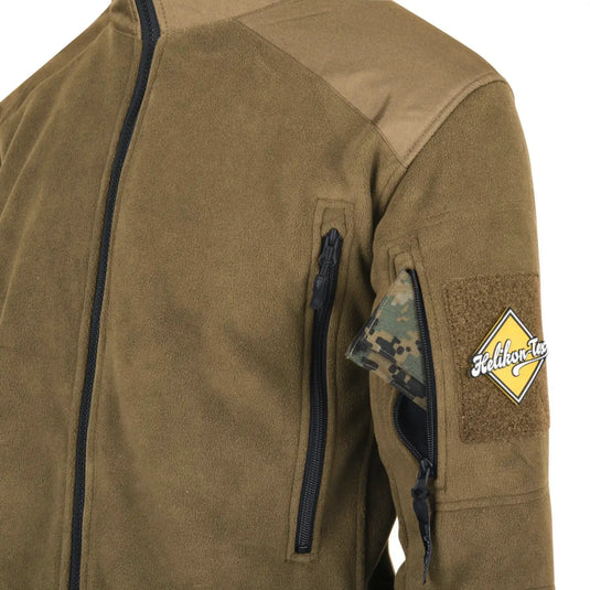 Nahaufnahme einer olivgrünen Helikon-Tex® Liberty Jacke – Double Fleece mit einer Schultertasche mit Reißverschluss und einem Aufnäher am Ärmel.