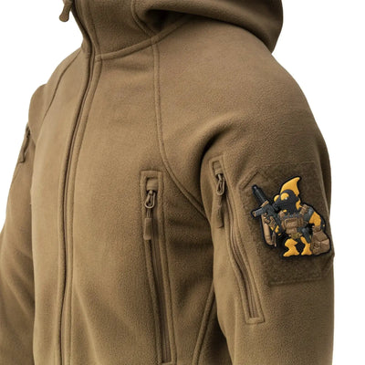 Eine Nahaufnahme einer Person, die eine Helikon-Tex® Patriot Jacket Mk 2 trägt und auf deren Ärmel ein kleiner Aufnäher mit einer animierten Figur mit einer Waffe befestigt ist.