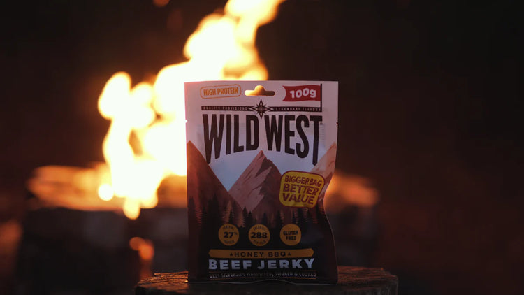 Eine Packung Wild-West-Honig-BBQ-Beef Jerky vor einem verschwommenen Lagerfeuer.