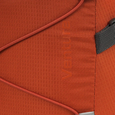 Nahaufnahme eines Abschnitts eines orangefarbenen HIGHLANDER® „VENTURE“-Rucksackmaterials mit dem eingeprägten Wort „venture“, einem Reißverschluss und einer genähten Naht.