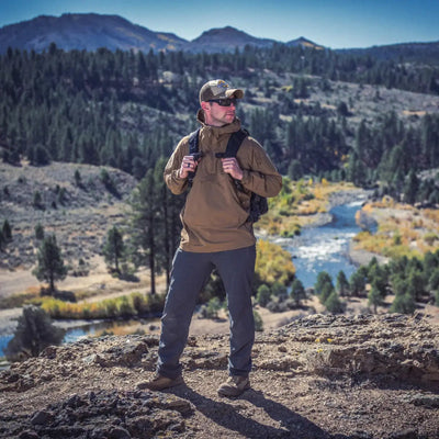 Wanderer, der eine Helikon-Tex® Mistral Anorak Jacket® trägt und innehält, um die Landschaft mit einem Fluss zu beobachten, der sich durch das bewaldete Tal darunter schlängelt.