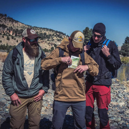 Drei Wanderer konsultieren im Freien eine Karte, einer trägt eine Helikon-Tex® Mistral Anorak Jacket®.