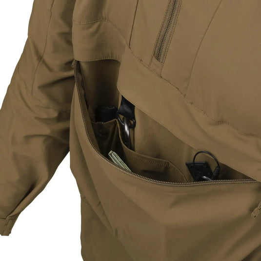 Nahaufnahme einer Reißverschlusstasche einer braunen Helikon-Tex® Mistral Anorak Jacket® mit Gegenständen darin.