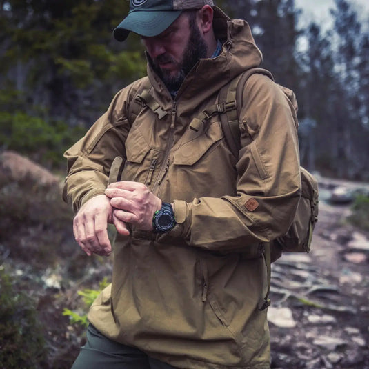 Mann in einer Helikon-Tex® Pilgrim Anorak-Jacke blickt auf einem Waldweg auf die Uhr.