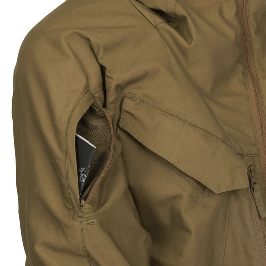 Nahaufnahme einer grünen Helikon-Tex® Pilgrim Anorak Jacke mit einem Smartphone in der Tasche.