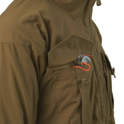 Nahaufnahme einer grünen Helikon-Tex® SAS Smock-Jackentasche mit einer Granate, die mit einer orangefarbenen Sicherheitsnadel gesichert ist.