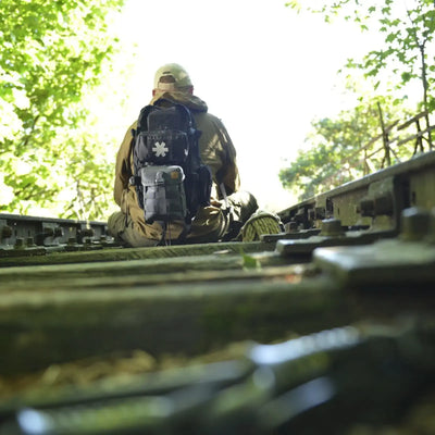 Eine Person in taktischer Ausrüstung und einem Helikon-Tex® RACCOON Mk2 Rucksack sitzt auf einer Bahnstrecke im Grünen.