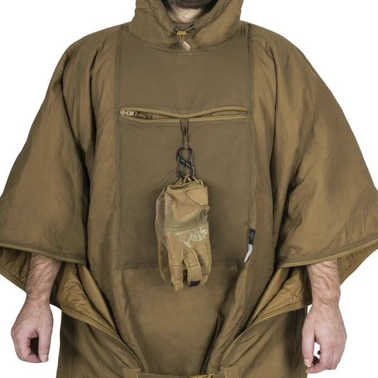 Person in einem braunen Helikon-Tex® Swagman Roll Poncho, der einen Handschuh hält.