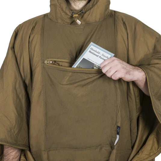 Eine Person hält einen „Franklin-Támesis-Nationalpark“-Reiseführer in der Tasche eines grünen Helikon-Tex® Swagman Roll Ponchos.