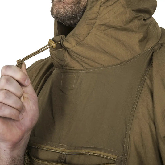 Mann justiert den Kordelzug an einem grünen Helikon-Tex® Swagman Roll Poncho mit Kapuze.