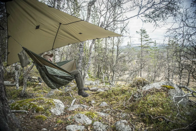 Person entspannt sich in einer Hängematte unter einer Plane in einem Waldgebiet.
