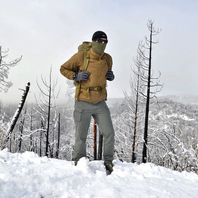 Ein Wanderer steht in einer verschneiten Landschaft mit kahlen Bäumen, gekleidet in Kaltwetterkleidung, darunter Helikon-Tex® VERSASTRETCH® Outdoor Tactical Pants.