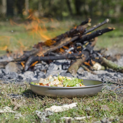 Im Vordergrund eine Schüssel Salat, im Hintergrund lodert ein Nordisk® Titan-Teller-Lagerfeuer.