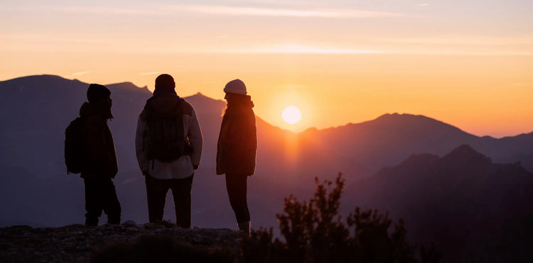 3 Menschen stehen beim Sonnenuntergang auf einem Berg