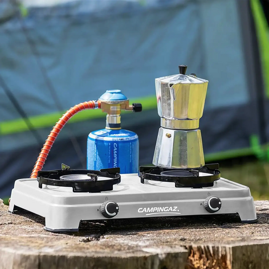 Tragbarer Campingkocher mit einer Kaffeemaschine oben, angeschlossen an eine Gasflasche, im Freien aufgestellt. Dieser Campingaz® Camping Cook CV, 3600 W ist perfekt für jeden Campingkoch.