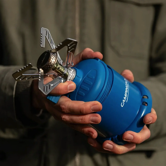 Eine Person hält einen kompakten, tragbaren Campingaz® Micro Plus 1250-W-Kocher mit einem blauen Brennstoffkanister.