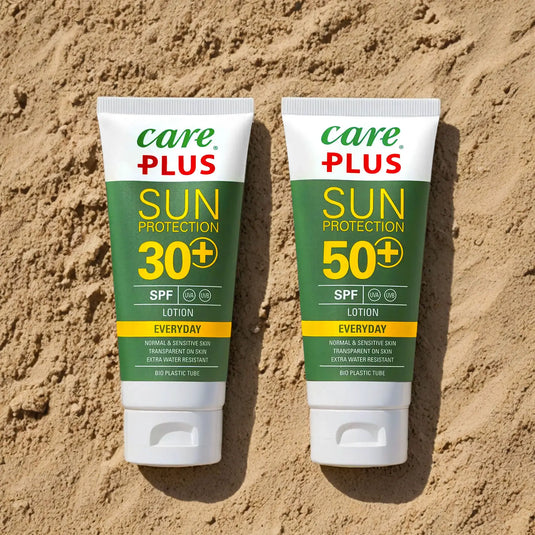 Care Plus® Sonnencreme Lotion 100ml Tuben auf sandigem Untergrund