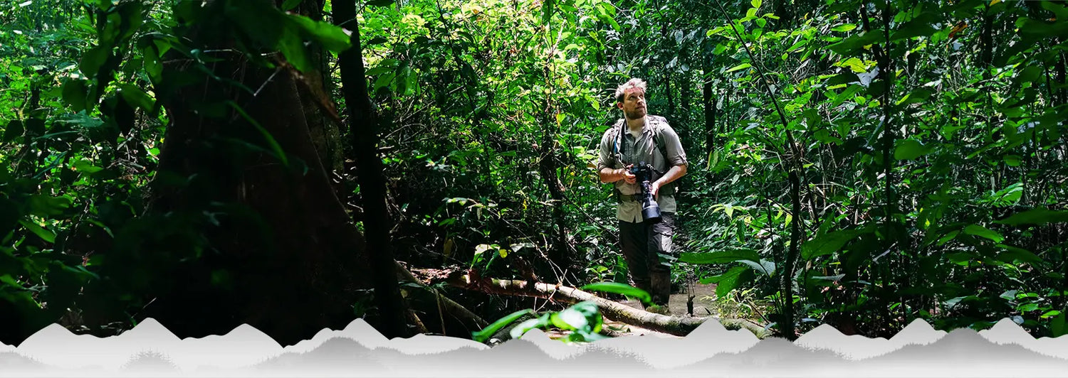 Mann mit Kamera beim Wandern in einem üppigen Wald, mit Text, der Kleidung vorschlägt, die Schutz vor beißenden Insekten bietet.