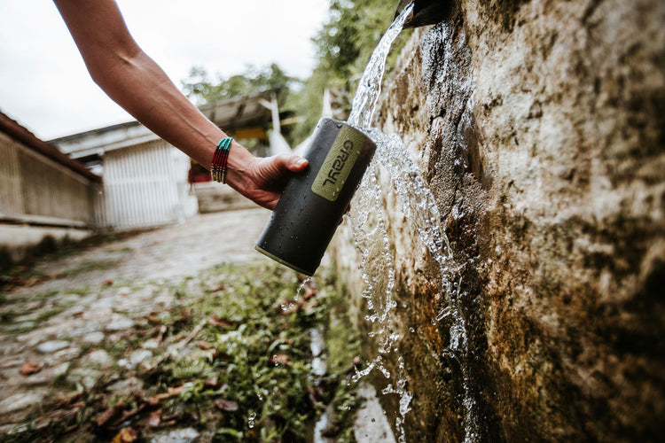 Füllen einer tragbaren Wasserflasche aus einem fließenden Steinbrunnen im Freien.