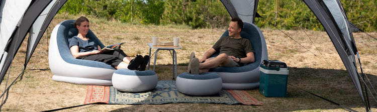 Zwei Personen entspannen sich in aufblasbaren Stühlen in einem Zelt auf einem Campingplatz.