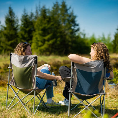 Zwei Personen unterhalten sich, während sie im Freien auf leichtgewichtigen, klappbaren Campingstühlen von Easy Camp® sitzen.
