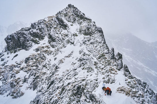 Bergsteiger erklimmt schneebedeckten, felsigen Berggipfel im Winter.