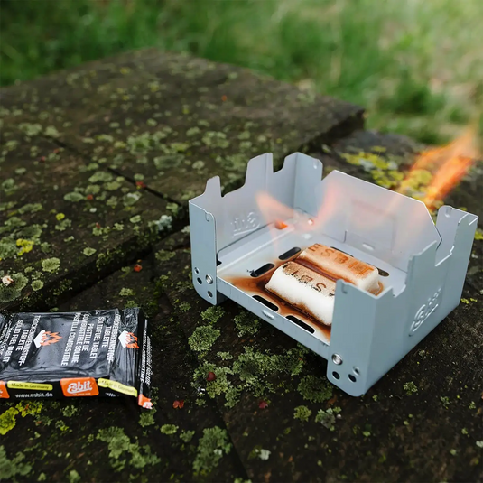 Tragbarer Herd mit brennender Flamme zum Kochen von Marshmallows auf einer Holzoberfläche im Freien, betrieben mit Esbit® Brennstofftabletten 8x27g.