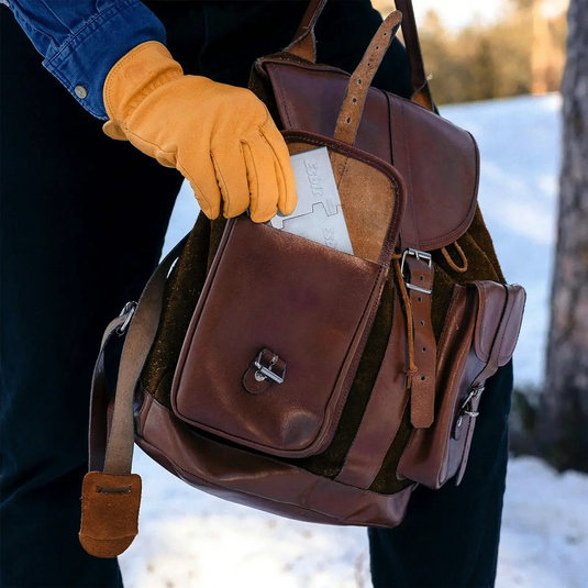 Eine Person, die einen gelben Handschuh trägt, hält einen Esbit® Brennstofftabletten 16x5g-Rucksack aus braunem Leder in einer verschneiten Outdoor-Abenteuerumgebung.