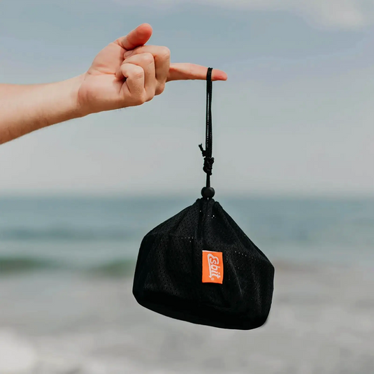 Eine Person hält einen schwarzen Beutel mit hitzebeständigem Esbit® Griffe, der an der Schlaufe aufgehängt ist, mit dem Meer im Hintergrund.