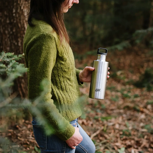 Frau hält eine auslaufsichere Esbit® Trinkflasche Sculptor 1000ml Edelstahl in einem bewaldeten Gebiet.