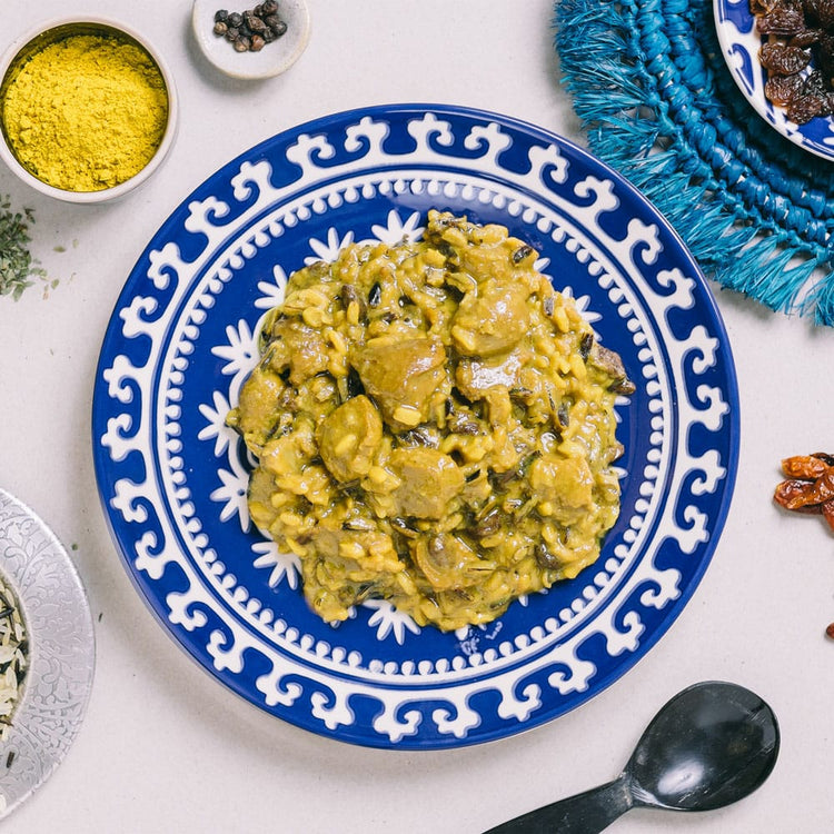 Ein Teller Curry, umgeben von Gewürzen und Dekorationsgegenständen auf einer Tischplatte.