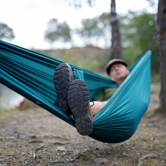 Eine Person, die sich draußen in einer Grand Canyon® Bass Hammock Double entspannt, die Füße gekreuzt und für die Kamera sichtbar.